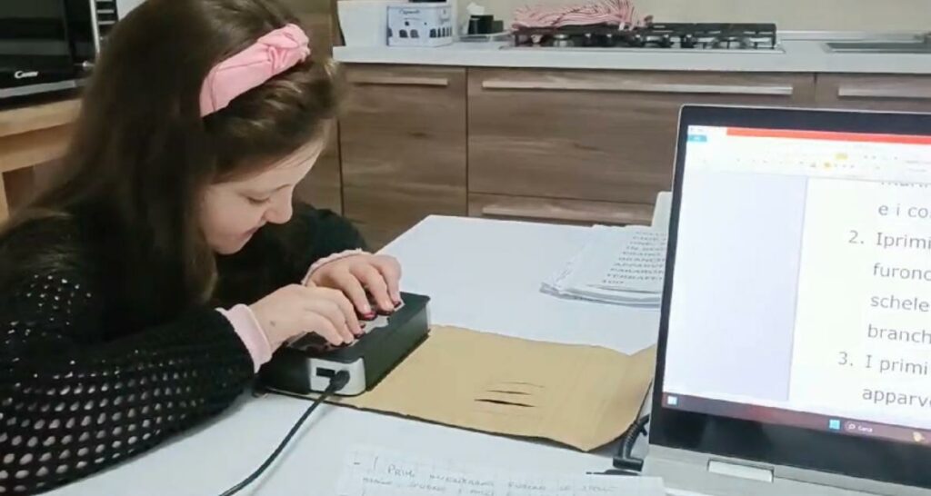 Una giovanissima studentessa legge un testo al computer con la barra Braille.
