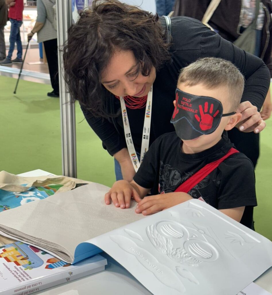 Giada Voce dell'Ufficio Stampa dell'UICI guida un bambino alla scoperta delle figure in rilievo con il tatto.