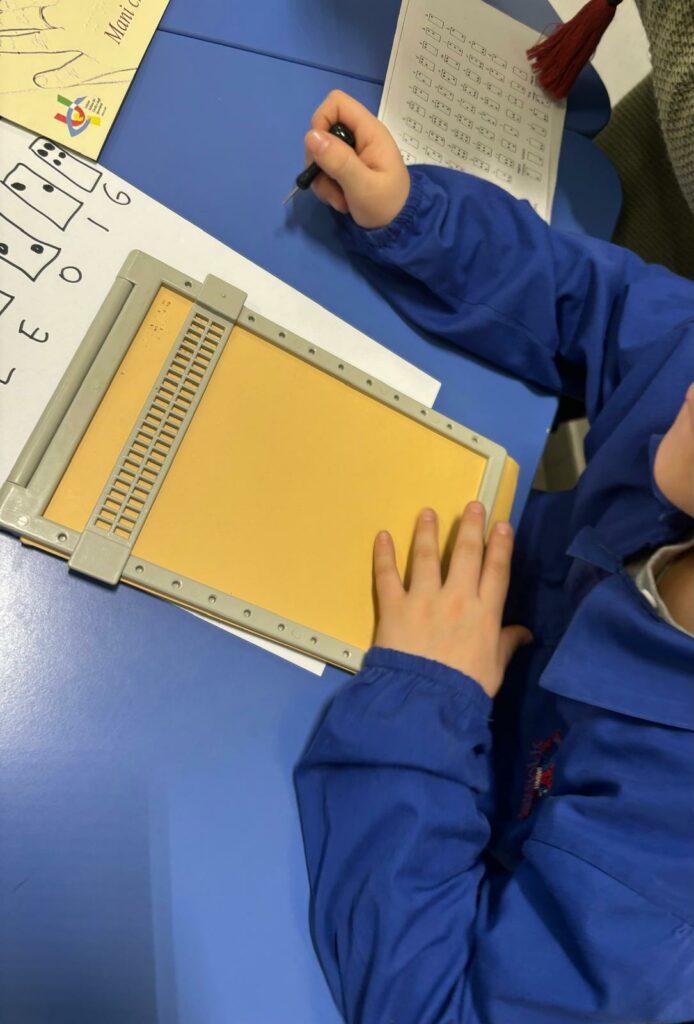 Un bambino è intento nell'apprendimento della scrittura Braille con l'ausilio della tavoletta. 